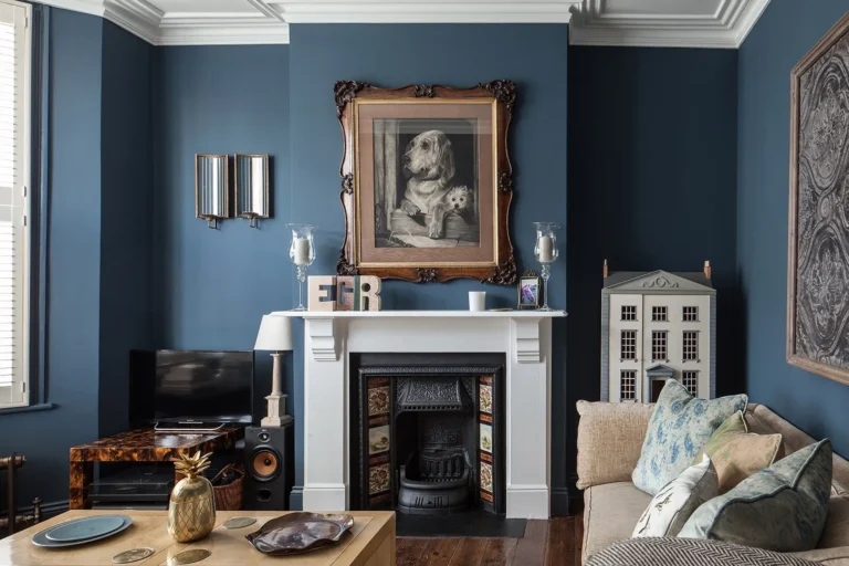 In a cozy Harringay living room with blue walls, a white fireplace adorned with decorative tile sits beneath a framed dog portrait. A beige sofa, small TV, and model house contribute to the eclectic decor of this charming home refurbishment.