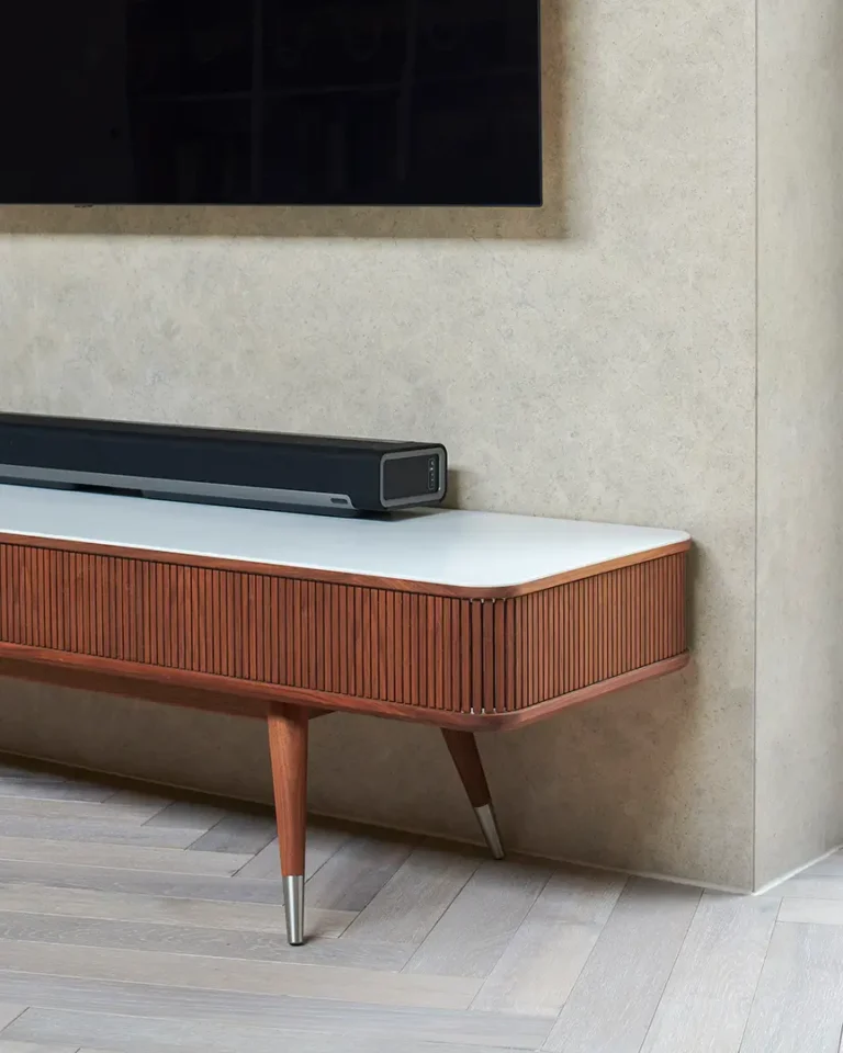 A sleek soundbar sits on a mid-century modern wooden TV stand, enhancing the interior design of the room. Above, a wall-mounted TV complements the space's aesthetic, while light wood flooring and a beige wall complete this stylish Muswell Hill home refurbishment.