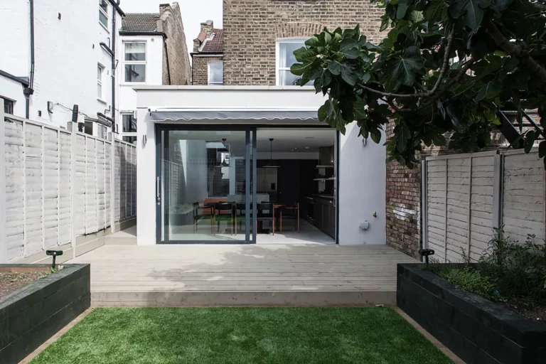 Modern home in the charming Harringay Ladder, featuring a glass sliding door that leads to a wooden deck and a small grassy yard, all surrounded by brick and wooden fences, seamlessly blending traditional North London architecture with contemporary design.