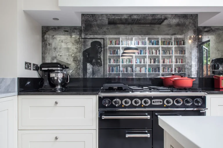 Modern kitchen designed by Trevor Brown Architect, featuring a black stove, red pots, and a mixer on the countertop with a reflective backsplash. Bookshelves in the background complete this stylish North London interior design.