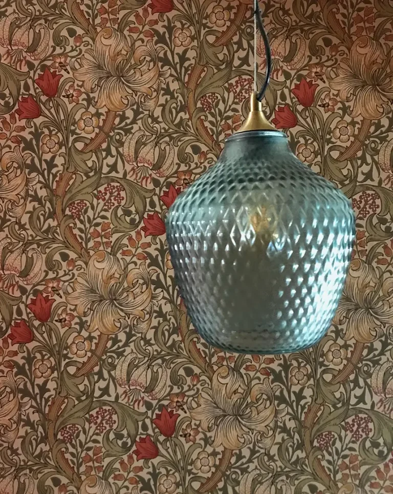 A textured glass pendant light elegantly hangs in front of floral wallpaper with red and beige tones, a testament to the meticulous home refurbishment by Trevor Brown Architect.