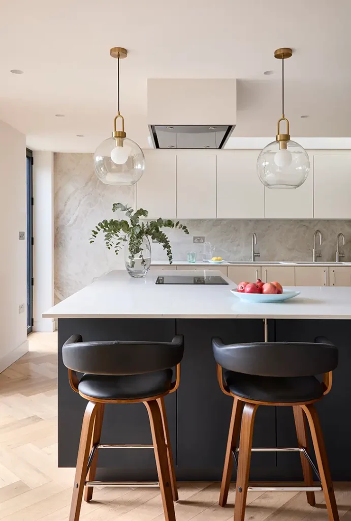 Trevor Brown Architect — Modern kitchen designed by Trevor Brown Architect, featuring a large island, two black bar stools, pendant lights, a vase with greenery, and a bowl of