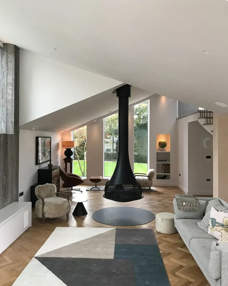 Modern living room by Trevor Brown Architect with a suspended black fireplace, geometric rug, grey sofa, armchair, wooden floor, and large windows overlooking a green garden—an inspiring interior design extension home refurbishment.